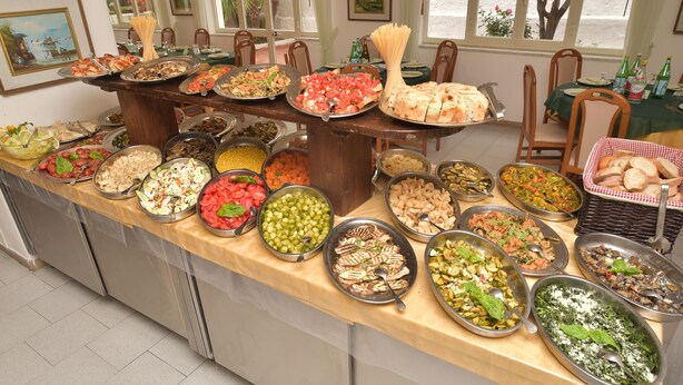 A buffet with various dishes and a table with chairs. - hotel park victoria (Forio)