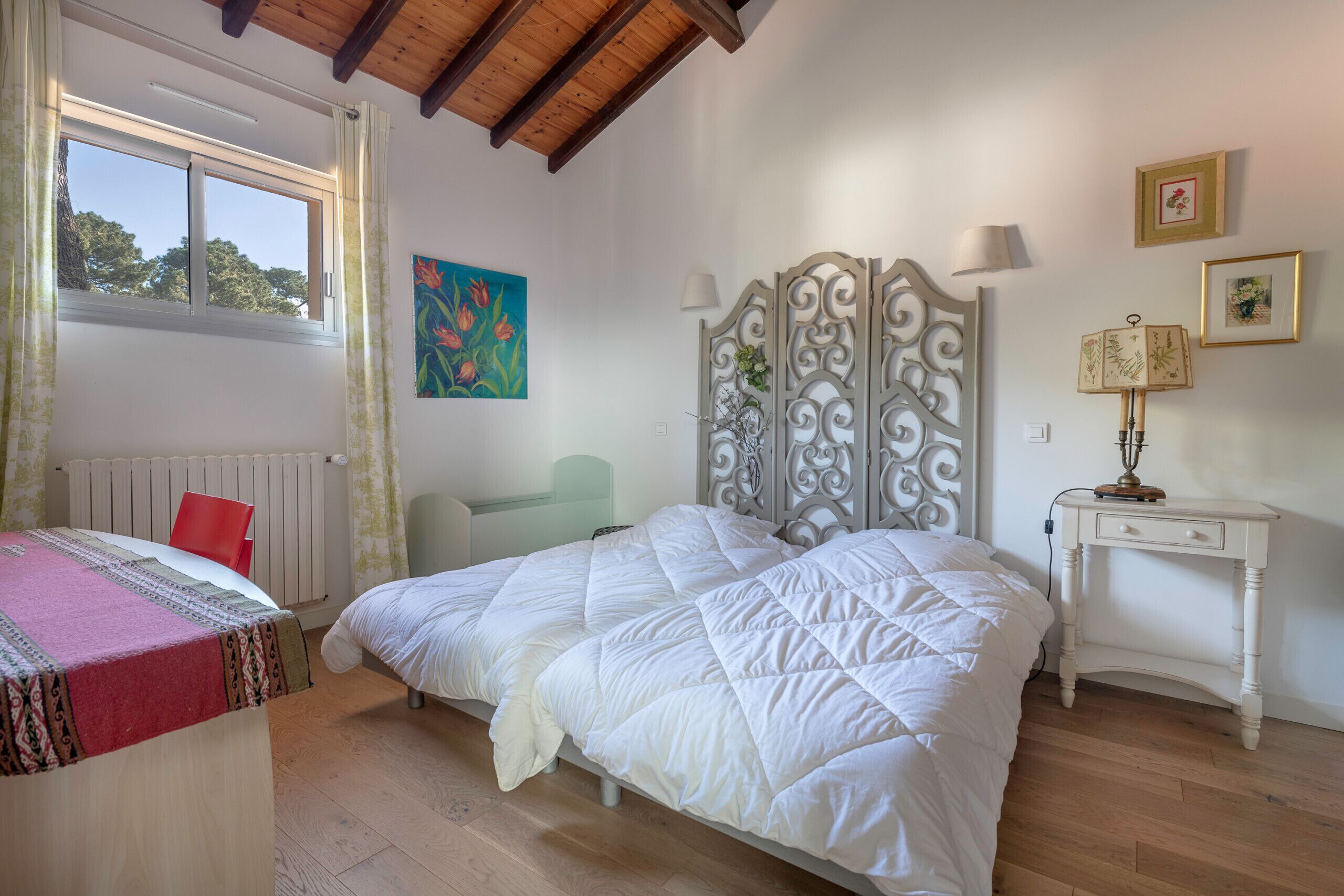 Ein Schlafzimmer mit einem großen Bett, einem Schreibtisch und einem Sessel. Es gibt ein Fenster mit Vorhängen, eine Heizung und ein Bild an der Wand.