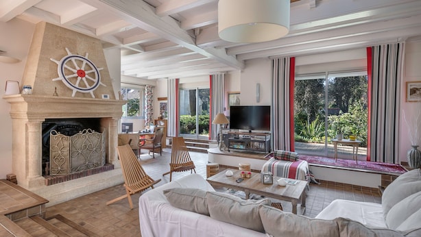 Un salón amplio con chimenea, asientos cómodos, televisión y ventanas grandes que ofrecen vistas al exterior.