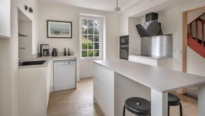 Una cocina moderna con armarios blancos, lavavajillas, microondas y una campana extractora de acero inoxidable.