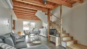 A modern living room with a gray sofa, wooden staircase, and a dining area with a table and chairs.