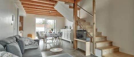 Un salon moderne avec un canapé gris, un escalier en bois et un coin repas comprenant une table et des chaises.