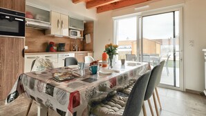 A modern kitchen with wooden beams, a dining area with a table set for four, and a sliding glass door leading to an outdoor patio.
