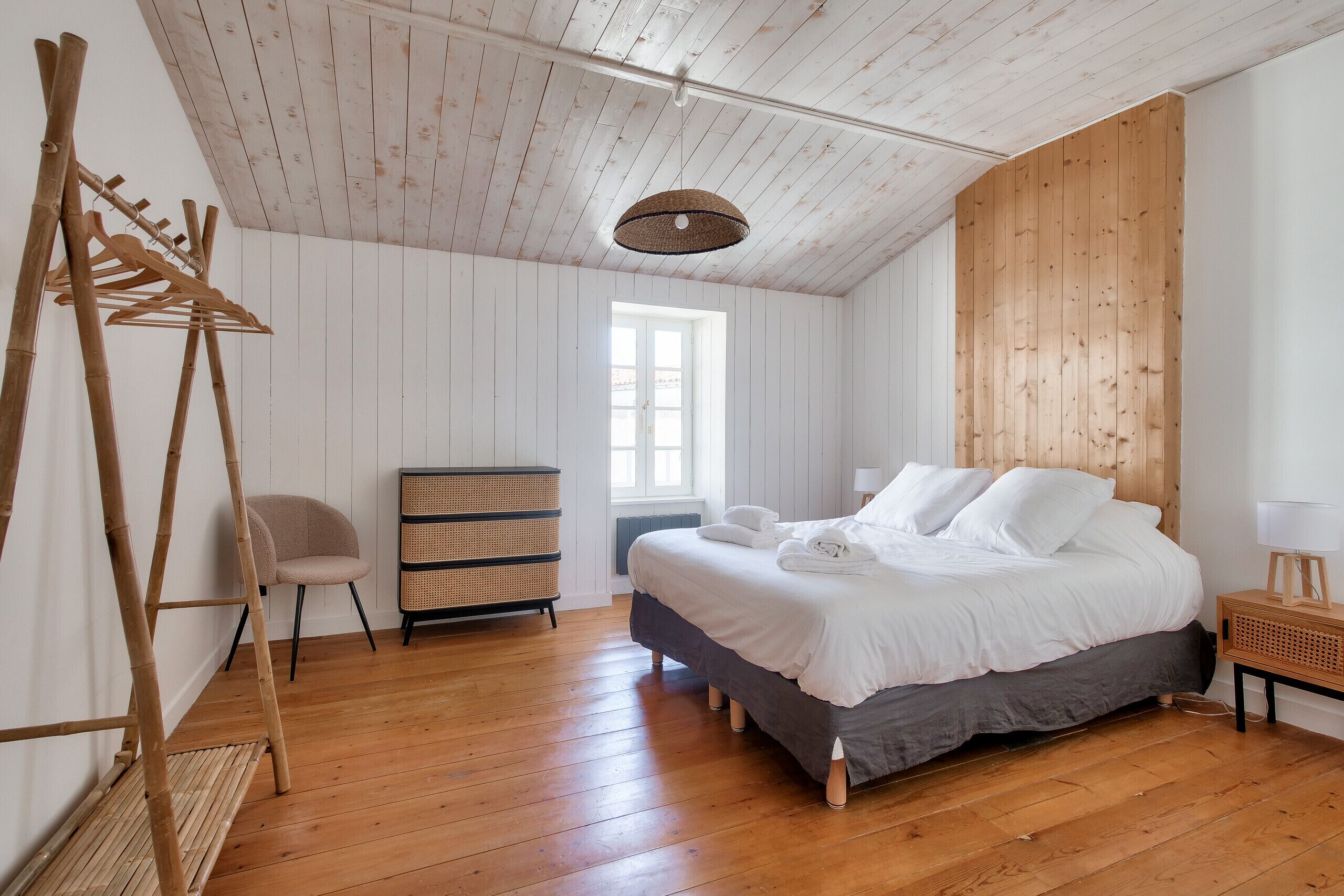 Ein Schlafzimmer mit Holzboden, einem Bett mit weißer Bettwäsche, einem Fenster und einer Hängeleuchte.