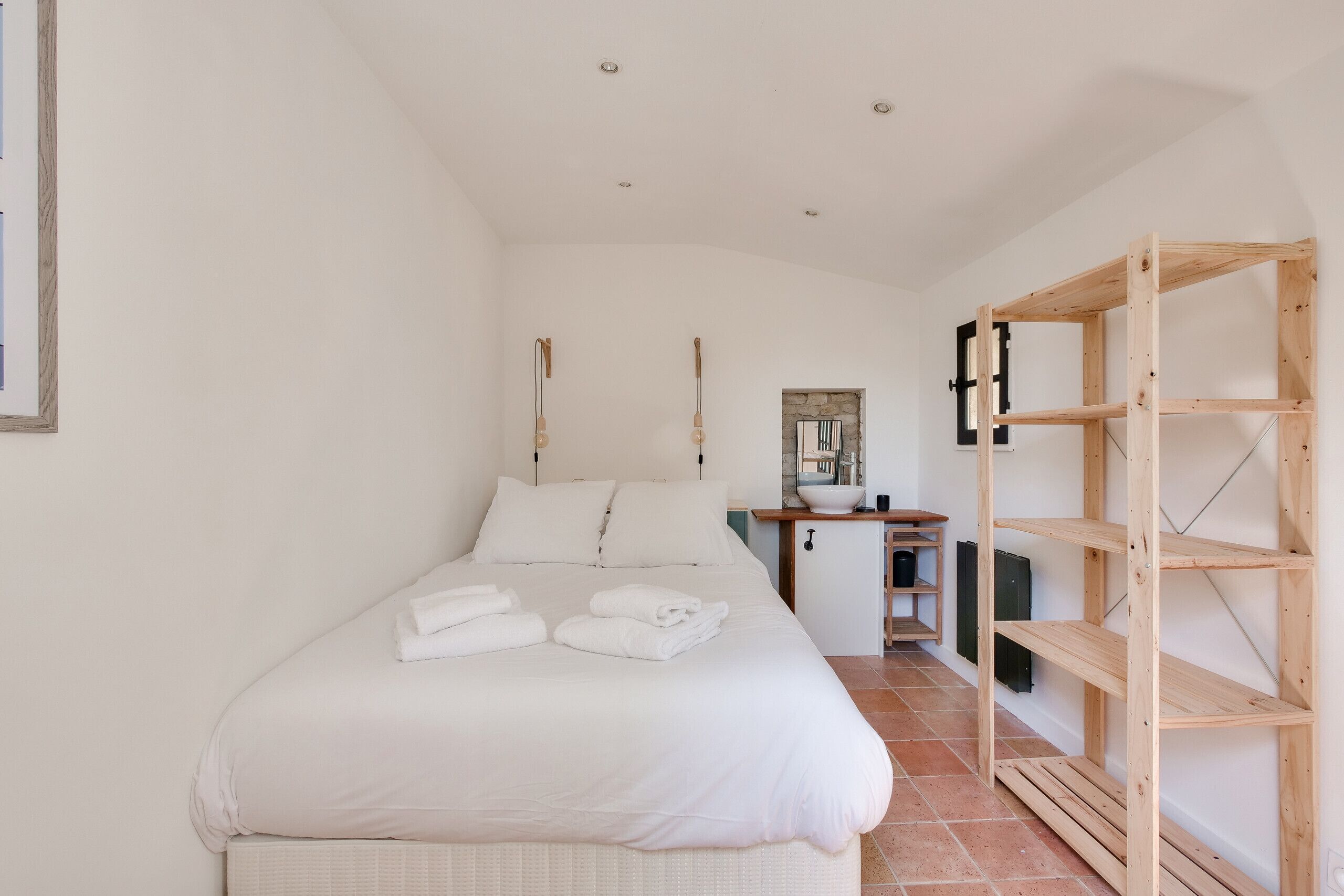 Un dormitorio con una cama, una estantería de madera y un escritorio pequeño con un espejo.