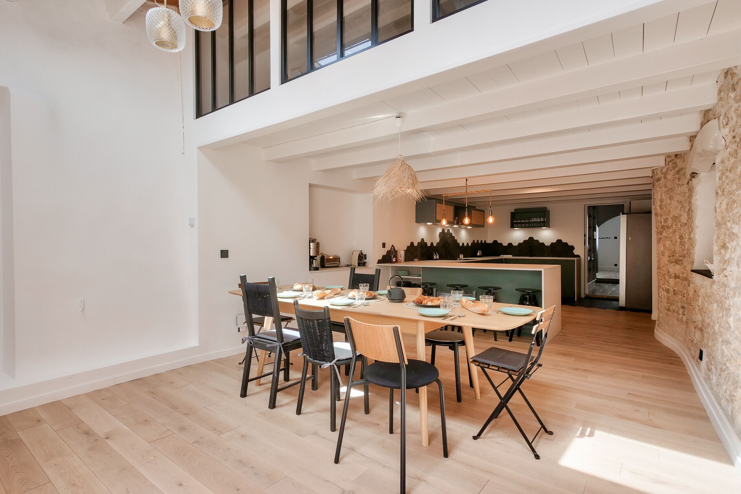Un comedor amplio con una mesa larga y sillas, una cocina al fondo y un techo alto con vigas a la vista.