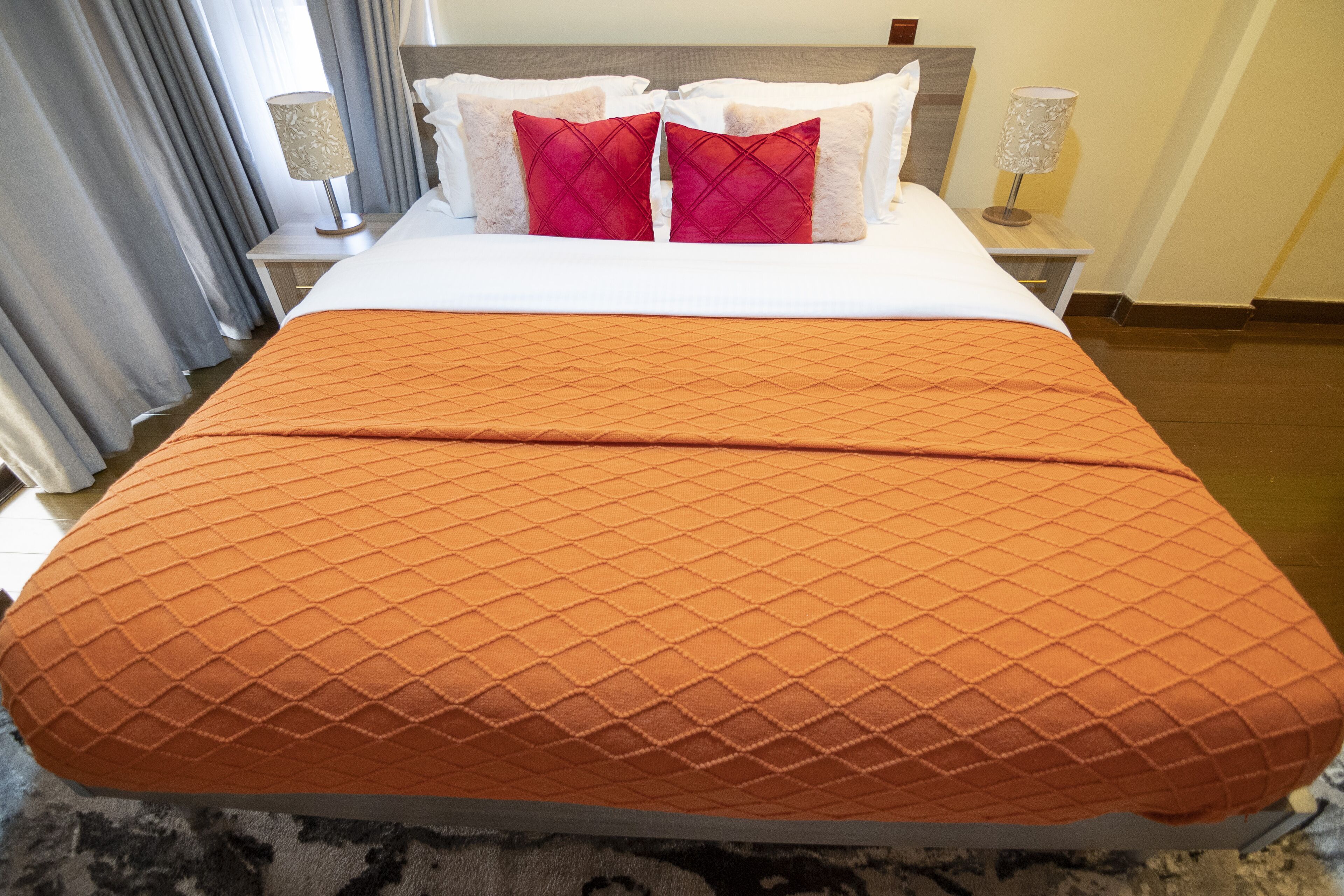 A neatly made bed with an orange quilt, white pillows, and a wooden headboard.