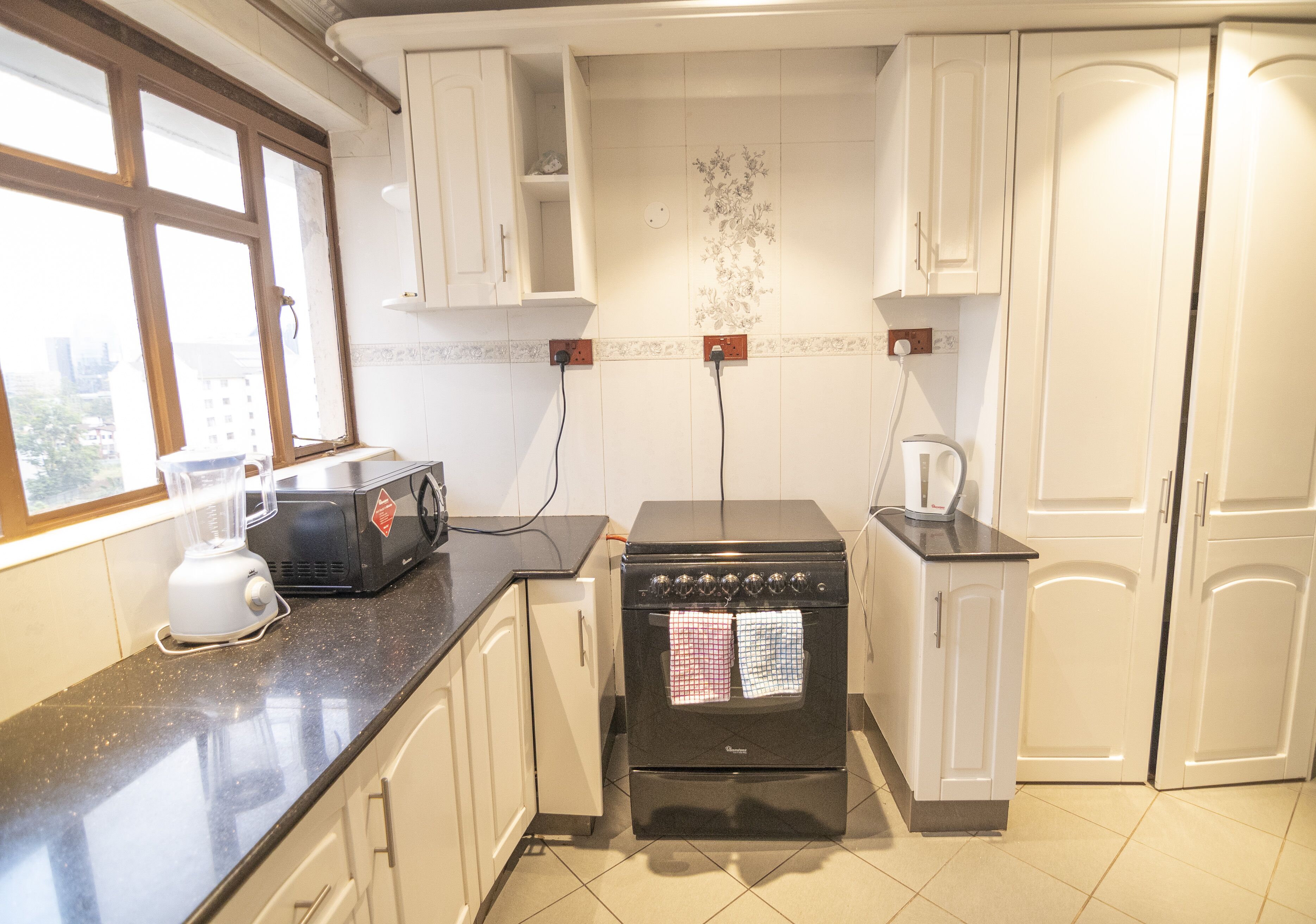 A kitchen with white cabinets, a black stove, a blender, and a window.