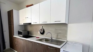 Una cocina moderna con armarios blancos, microondas integrado, un lavamanos y un refrigerador compacto.