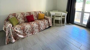 Una habitación con sofá, mesa de comedor y ventana con cortinas.