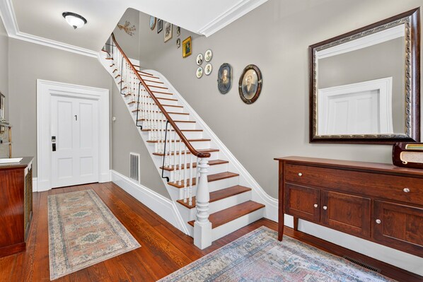 A staircase with wooden steps and white railings, a wooden dresser, a large mirror, and a door labeled '1'. - York Street Living! Off-Street Parking Spot!! (Savannah)