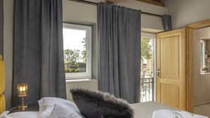 Ein Schlafzimmer mit einem Bett, grauen Vorhängen, einem Fenster, einer Holztür und einer Nachttischlampe.