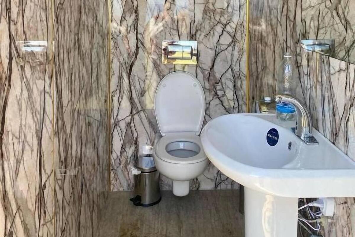 Een badkamer met een marmeren wand, een toilet, een wastafel en een spiegel.
