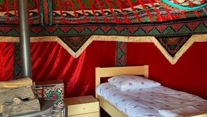 Een gezellige kamer met een bed, een klein houten dressoir, een verwarming en een kamerkleed met een patroon.