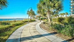 A curved pathway leading to a beach with palm trees and a clear blue sky. - Budget Friendly Condo for 2 in Myrtle Beach, Walk to the Waves! (Myrtle Beach)
