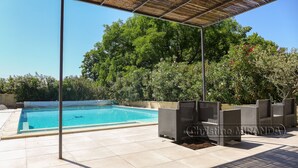 En pool med et pergolaoverdækket område, omgivet af frodig vegetation.