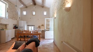 Et rummeligt køkken med spiseplads, stenvægge og et rustikt bjælkebefængt loft.