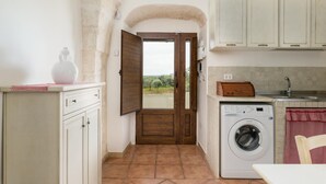 A compact kitchen with a washing machine, a sink, and a view through an open door. - Ilarius Country House by Wonderful Italy (Ostuni)