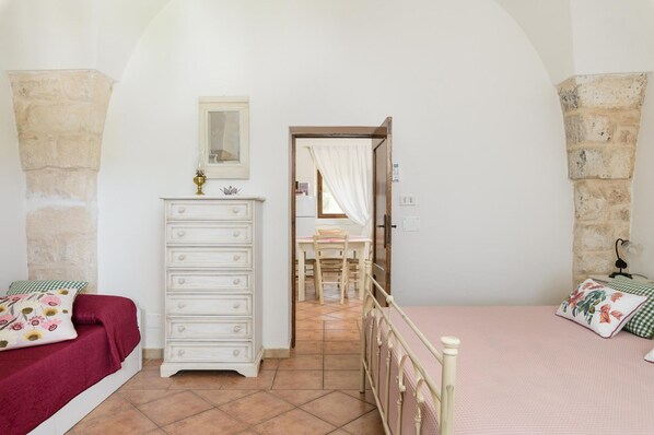 A bedroom with a bed, dresser, and a view into another room.