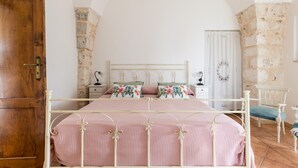 A bedroom with a bed, a wooden door, a stone wall, and a white curtain. - Ilarius Country House by Wonderful Italy (Ostuni)