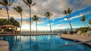 A swimming pool with lounge chairs and palm trees, surrounded by a fence and a view of the ocean. - Polo Beach Club 106 | Beachfront Wailea Condo with Direct Beach Access (Wailea)