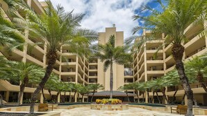 A multi-story hotel with a central courtyard featuring palm trees, a swimming pool, and outdoor seating. - Polo Beach Club 106 | Beachfront Wailea Condo with Direct Beach Access (Wailea)