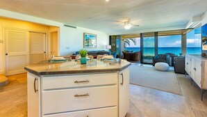 A modern kitchen with a large island, a dining area with a view of the ocean, and a living room with a sofa and a coffee table. - Polo Beach Club 106 | Beachfront Wailea Condo with Direct Beach Access (Wailea)