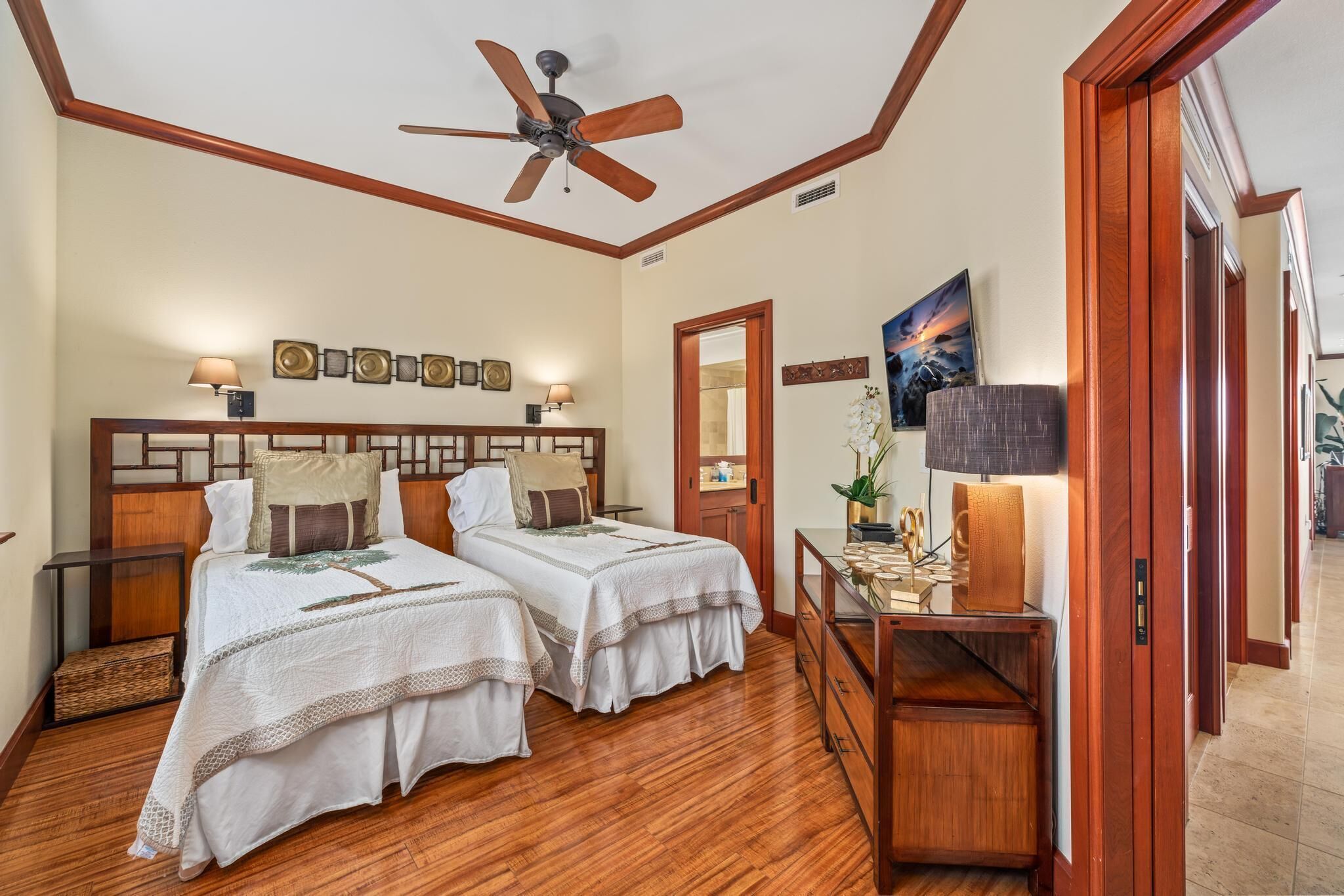A hotel room with two beds, wooden headboards, a ceiling fan, a nightstand with a lamp, a dresser, and a mirror.