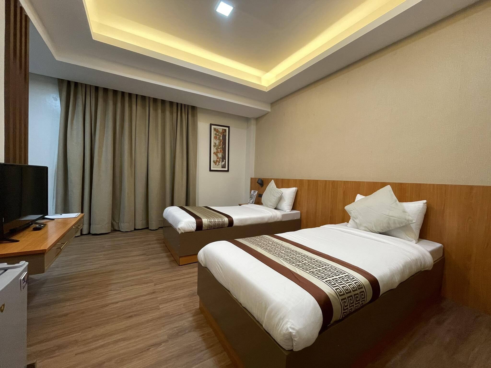 A hotel room with two beds, a desk, a television, and a large window with curtains.