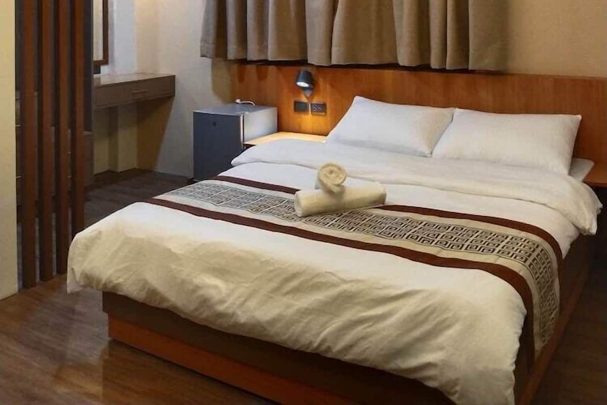 Une chambre d’hôtel avec un lit, une table de chevet, une lampe et des rideaux.
