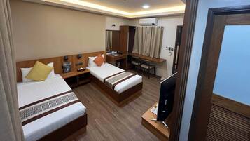 A hotel room with two beds, a desk, a TV, and an air conditioning unit.