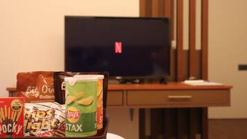 A room with a TV displaying a Netflix logo, snacks including Lay's STAX and Rocky Light, and a wooden desk.