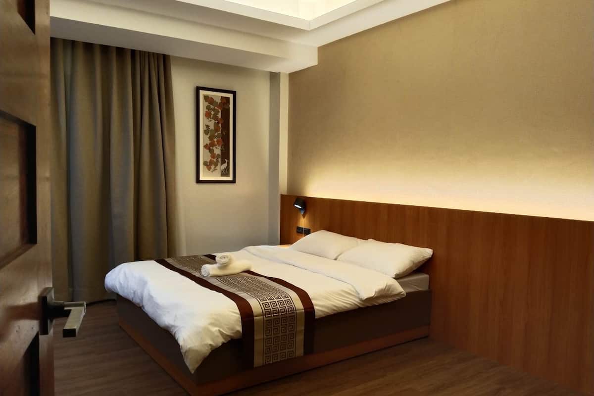 Une chambre d’hôtel avec un lit, une tête de lit, une table de chevet, une lampe, un tableau encadré et une fenêtre avec des rideaux.