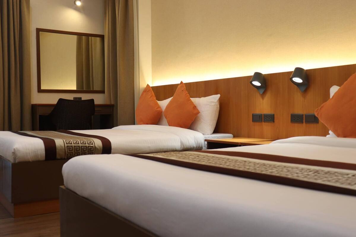 Une chambre d’hôtel avec deux lits, un grand miroir et une tête de lit en bois agrémentée de lampes fixées au mur.