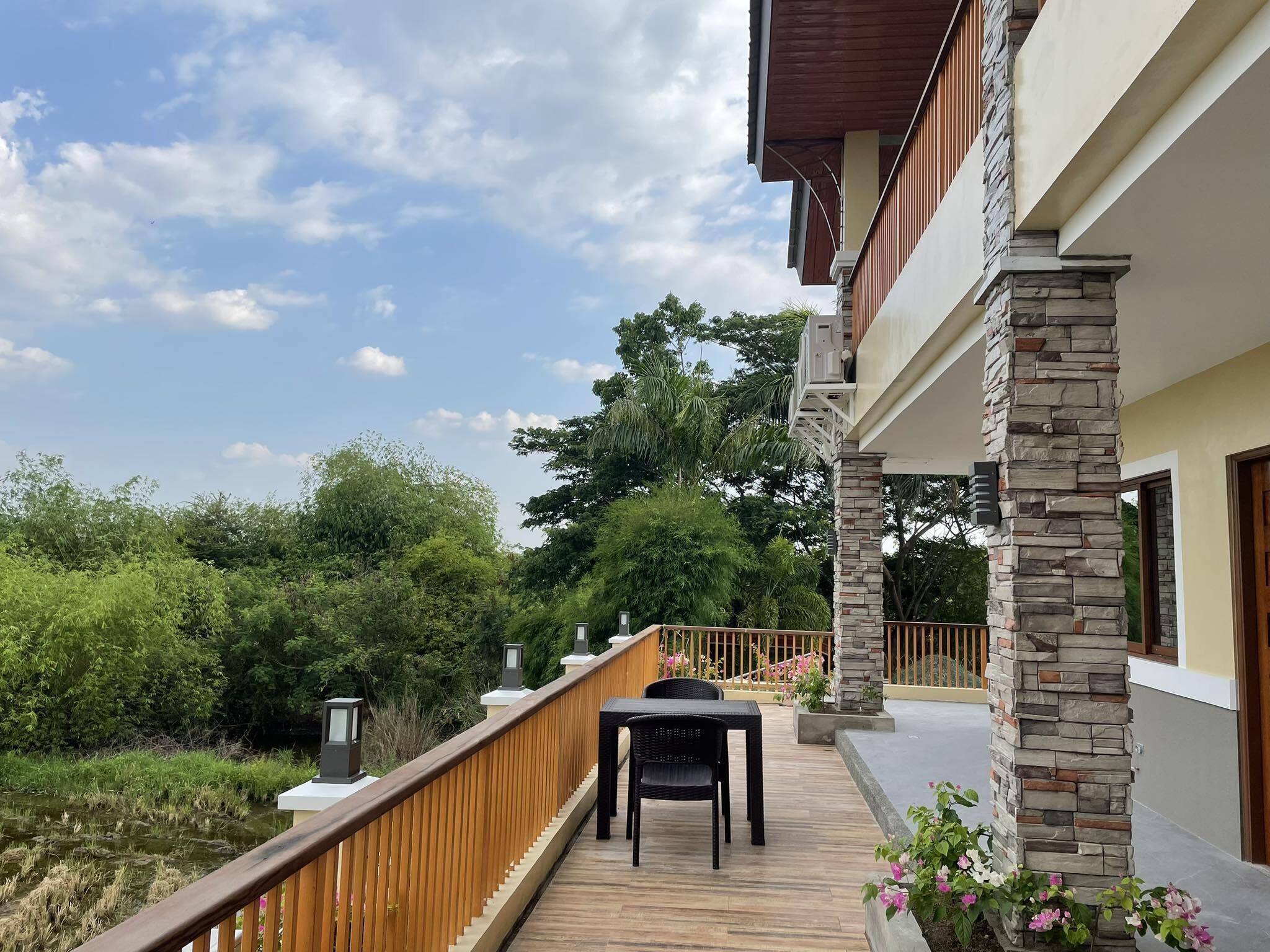 A wooden deck with a table and chairs, a stone pillar, and a view of greenery and trees.