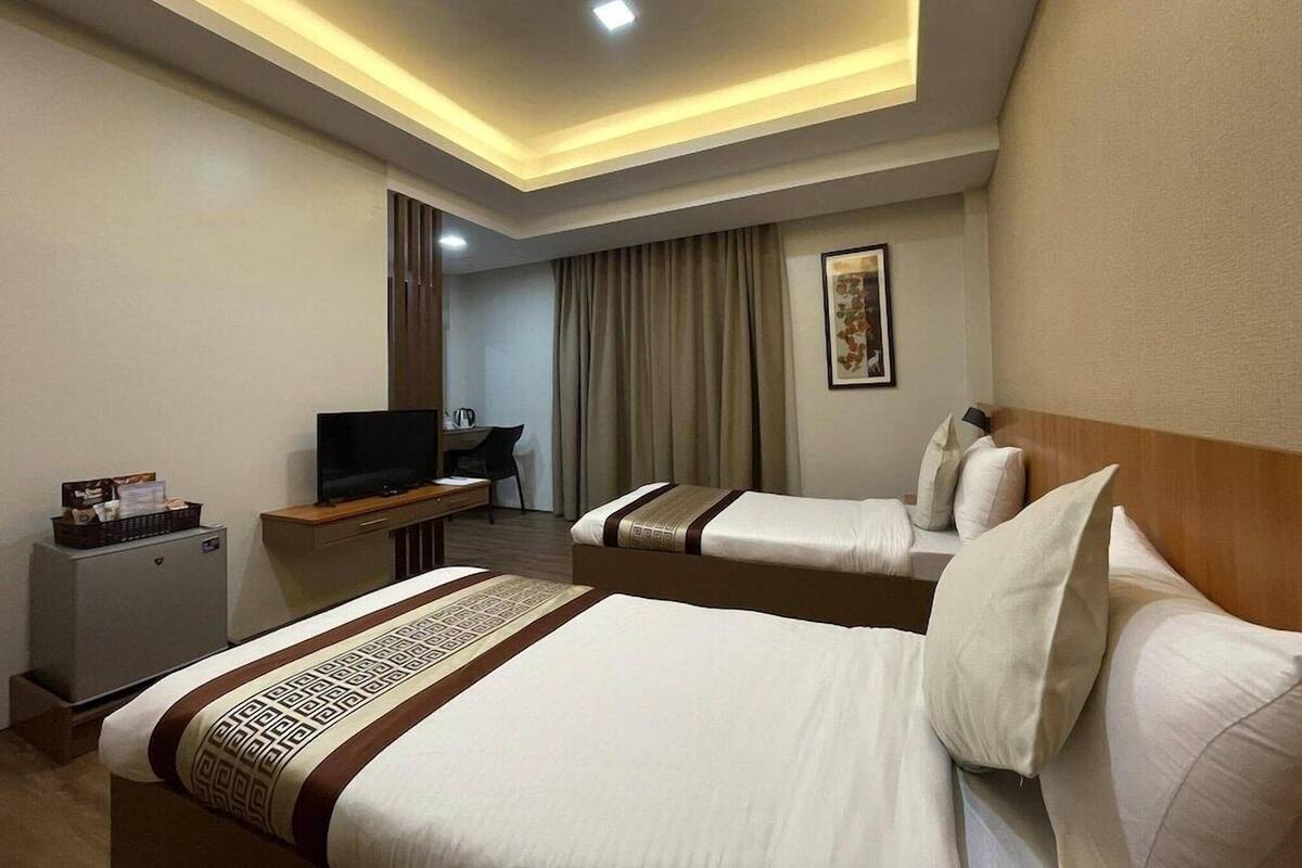 Une chambre d’hôtel avec deux lits, un bureau avec une télévision, une petite armoire et un luminaire au plafond.