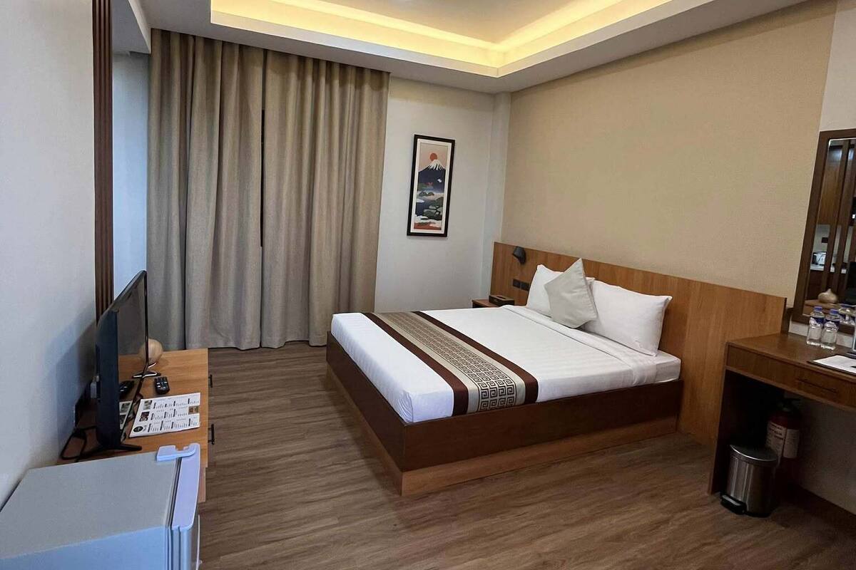 Une chambre d’hôtel équipée d’un lit, d’un bureau avec un ordinateur, d’une télévision et d’une petite poubelle.