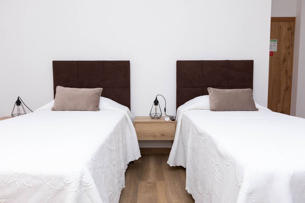 Ein Doppelzimmer mit zwei Einzelbetten, jeweils mit einem Nachttisch und einer Lampe.