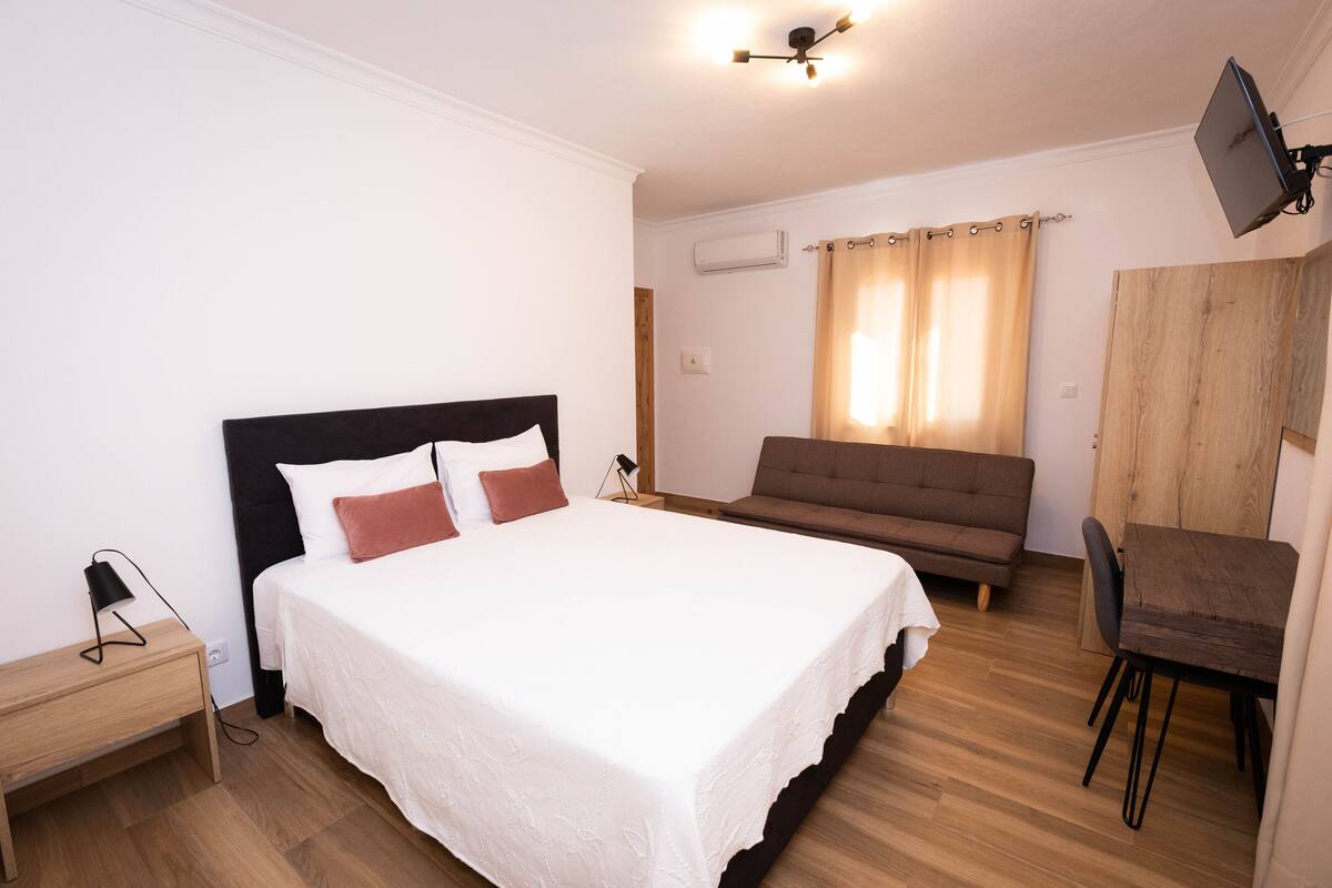 Ein Schlafzimmer mit einem Bett, einem Holztisch, einer Couch und einem an der Wand befestigten Fernseher.