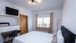 Une chambre à coucher avec un lit, un bureau, une chaise, une télévision et une fenêtre avec des rideaux.