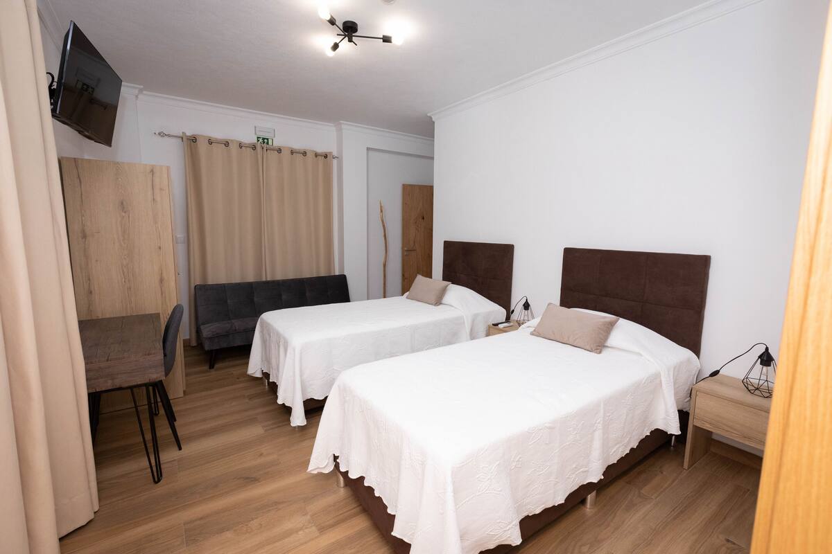 Ein Hotelzimmer mit zwei Einzelbetten, einem Schreibtisch, einem Stuhl, einem Fernseher und einer Deckenleuchte.