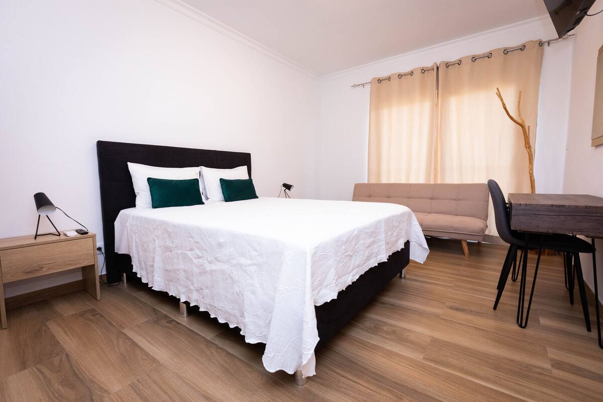 Ein ordentlich eingerichtetes Schlafzimmer mit Bett, Nachttisch und kleinem Schreibtisch.