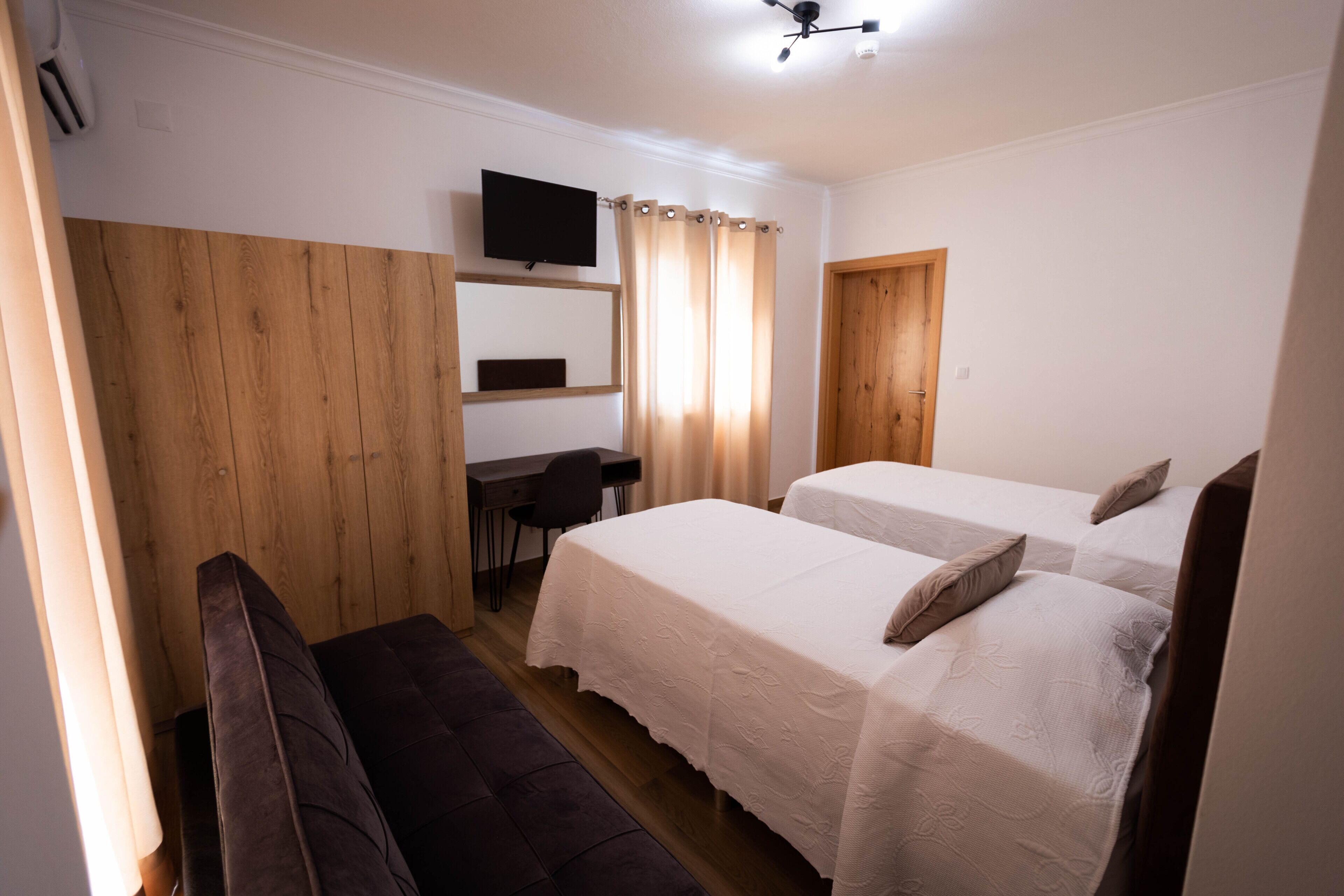 Un dormitorio con dos camas, un escritorio, una silla y un televisor en la pared.