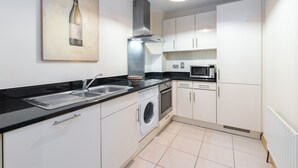 A modern kitchen with white cabinets, a stainless steel range hood, a built-in microwave, and a washing machine. - Charming Leopardstown Townhouse (Dublin)