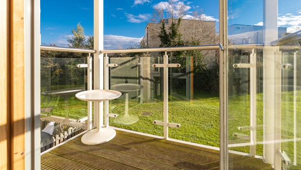 A modern room with large glass windows, a wooden floor, and a small round table. - Charming Leopardstown Townhouse (Dublin)