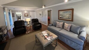 A spacious living room with a grey couch, a coffee table with magazines, and a dining area with a chandelier.