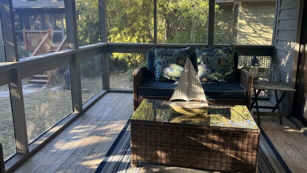 A covered porch with a wicker sofa, a small table, and a view of a backyard.