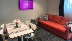 Quarto moderno com sofá vermelho, TV na parede, mesa de jantar com cadeiras e uma pequena mesa lateral.