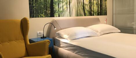 A hotel room with a bed, a chair, a nightstand, and a wall-mounted painting of a forest.