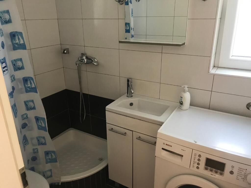 Une petite salle de bain équipée d’une douche, d’un lavabo et d’un lave-linge.